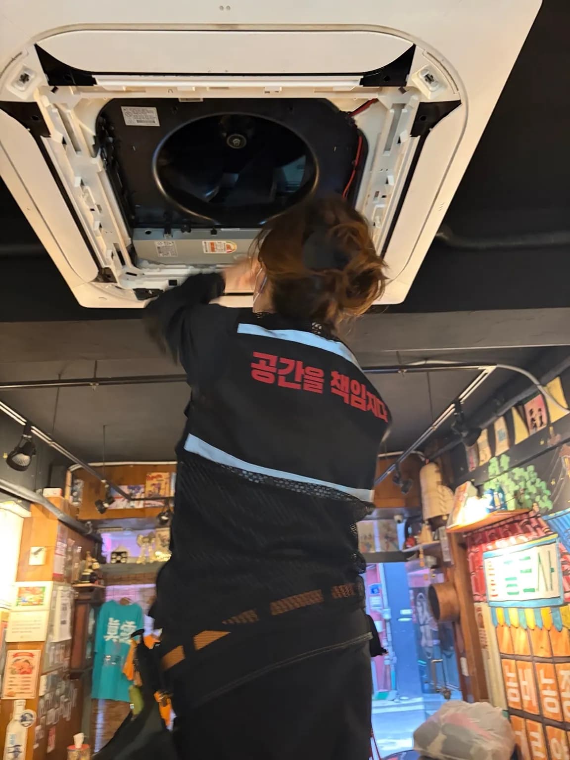 사다리에 올라 천장형 에어컨 내부를 분해해 청소하는 작업자