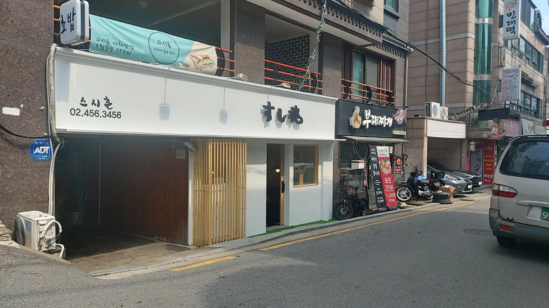 흰색 사인과 목재 루버 파사드로 마감한 스시 전문점 외관과 오픈 안내 현수막