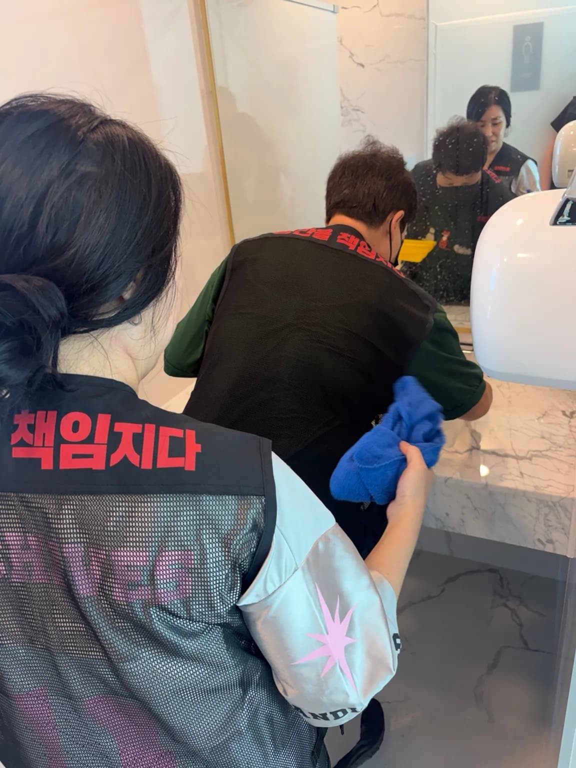 세면대 앞 거울과 수전 주변을 닦고 있는 작업자