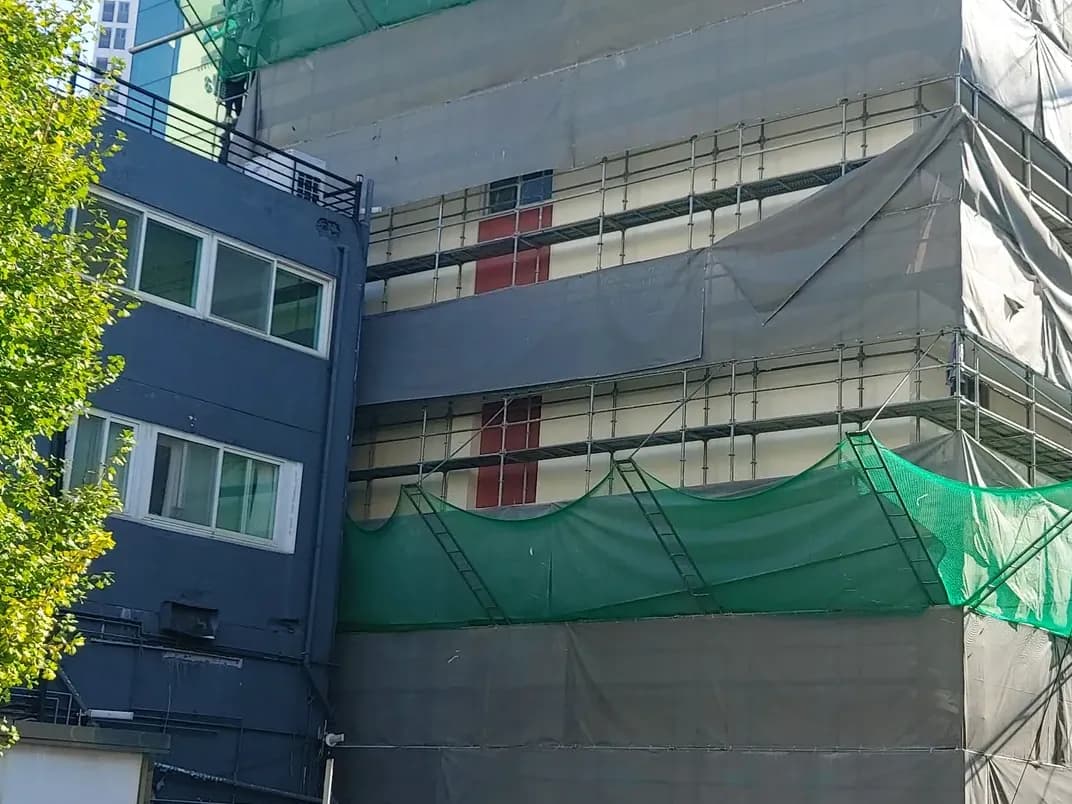 녹색 안전망과 회색 보양막으로 층별로 감싼 건물 외벽